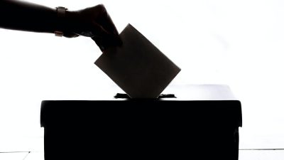 A hand placing a ballot into a ballot box
