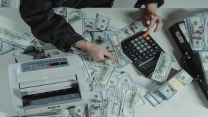 Person using a calculator that is on a desk with a large sum of money on it