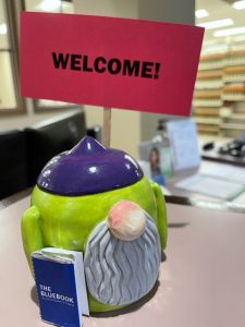 A ceramic gnome holding a welcome sign and a bluebook.